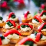 A side view of a platter filled with small toasted crostinis topped with a bean purée, sautéd spinach, and a strip of roasted red bell pepper.