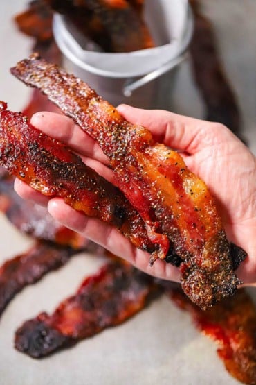 A person holding two strips of maple pepper bacon in the palm of his hand.