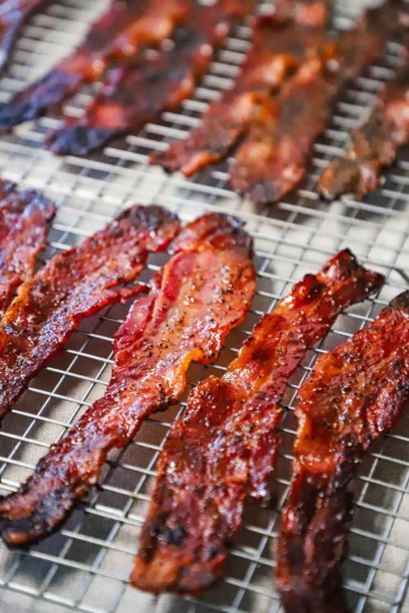 A straight-on view of cooked strips of maple pepper bacon resting on two baking racks.