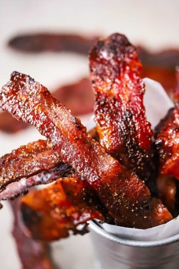 A close-up view of cooked strips of crispy maple pepper bacon sitting in a small silver pale lined with white butcher paper.