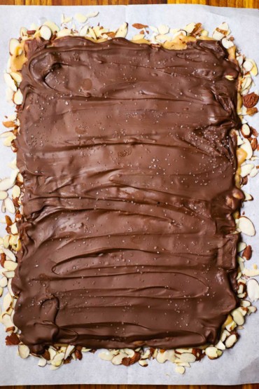 An overhead view of a rectangular shape of sliced almonds topped with toffee and then melted chocolate.
