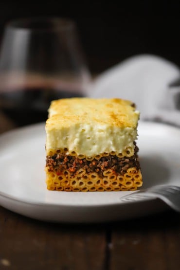 A straight-on view of a perfectly square piece of Greek pastitsio on a white dinner plate.