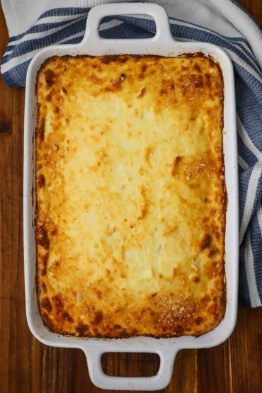 An overhead view of a large white lasagna dish filled with a casserole that is topped with a browned Greek bechamel sauce.