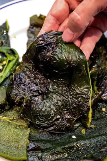 A person holding up a poblano pepper that has been roasted and cut open with the seeds removed.