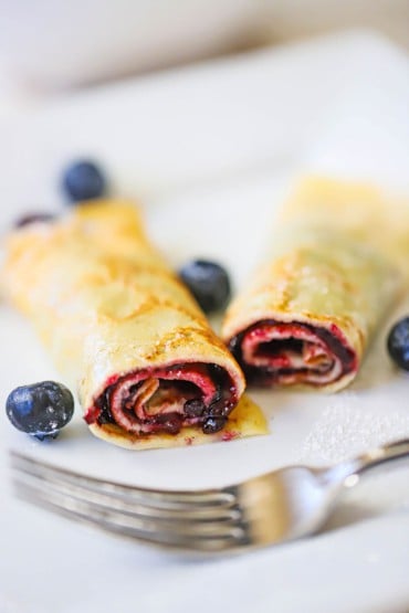 A close-up view a rolled Norwegian pancake the has been filled with blueberry jam and then cut in half so the insides are revealed.