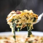 A close-up view of a large spoon lifting up a steaming helping of wild rice, spinach, and fontina casserole.