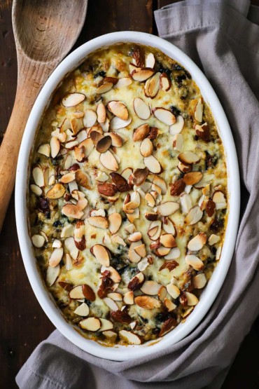 An overhead view of a baked casserole that is topped with melty fontina cheese and lightly browned almond slivers.