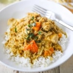 A straight-on view of a white bowl filled with a serving of slow-cooker coconut chicken curry with a glass of white wine nearby.