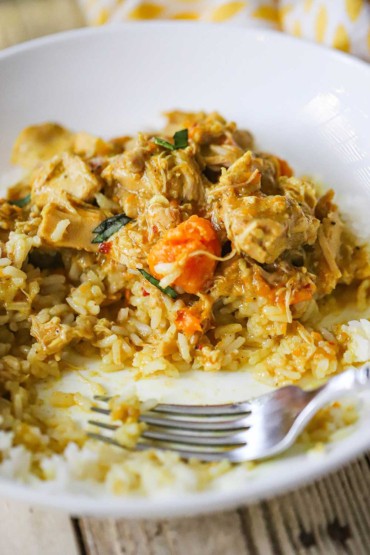 A close-up view of a white bowl filled with a half-eaten portion of slow-cooker coconut chicken curry with chunks of tender carrots and sweet potatoes.