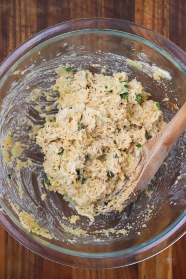 An overhead view of a crab and herbs mixture in a glass bowl with a wooden spoon inserted in the side.