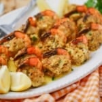 A close-up view of a white platter filled with crab-stuffed shrimp with lemon wedges nearby.