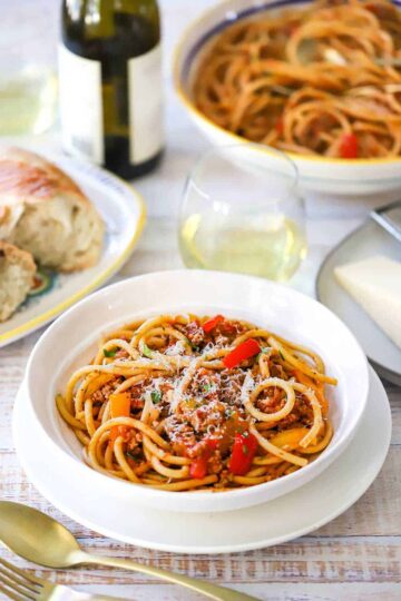 A straight-on view of a white pasta bowl that is full of pasta with turkey and sweet pepper ragu topped with freshly grated parmesan cheese.