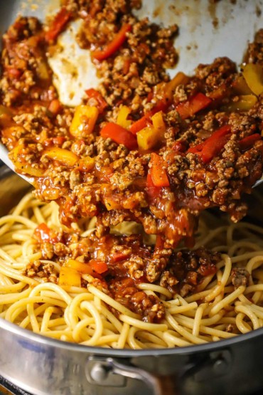 A turkey and sweet pepper ragu being transferred from one skillet into another skillet that is filled with cooked bucatini pasta.