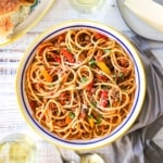 An overhead view of a large pasta bowl filled with pasta with turkey and sweet pepper ragu and surrounded by a glass of white wine and Italian bread.