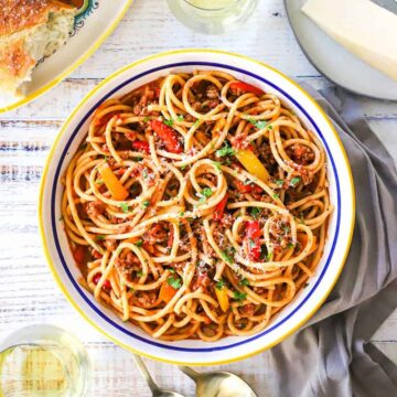 An overhead view of a large pasta bowl filled with pasta with turkey and sweet pepper ragu and surrounded by a glass of white wine and Italian bread.