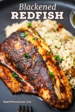 A close-up view of a blackened redfish filet resting on a bed of rice pilaf on a black dinner plate.