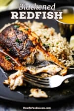 A close-up view of a half-eaten blackened redfish sitting on a black dinner plate also filled with rice pilaf and small vessel of melted butter.