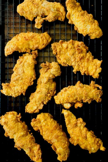 An overhead view of a about ten crispy chicken tenders sitting on a baking rack over a baking sheet.