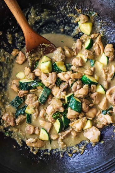 An overhead view of a wok filled with Thai green curry chicken with a large wooden spoon inserted on the side.