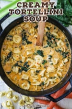 An overhead view of a black cast-iron pot filled with creamy tortellini soup with sausage and spinach.