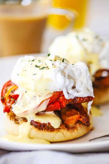 A close-up view of an egg blackstone sitting on a white plate with hollandaise sauce drizzled over the top and on the plate.
