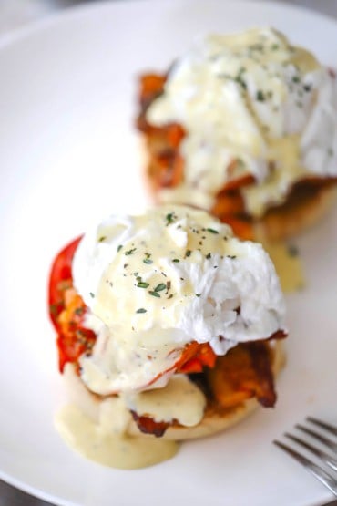 An overhead view of two servings of eggs blackstone which consists of two English muffins topped with bacon, roasted tomatoes, poaches eggs, and hollandaise sauce.