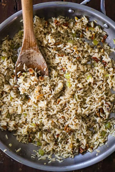 An overhead view of a large silver skillet filled with a herbed rice pilaf with toasted pecans.
