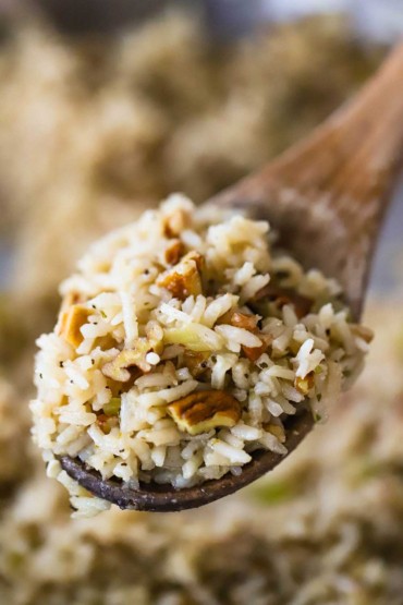 A large wooden spoon holding up a serving of herbed rice pilaf with toasted pecans.