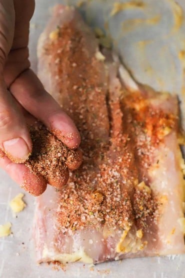 A person using his fingers to press a blackening rub into an uncooked filet of redfish.