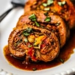 A close-up view of slices of flank steak that is stuffed with carrots, peppers, onions, and herbs and topped with a brown sauce.