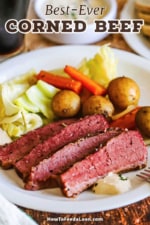 A dinner plate filled with a serving of slices of corned beef and cabbage with cooked baby potatoes and carrots.