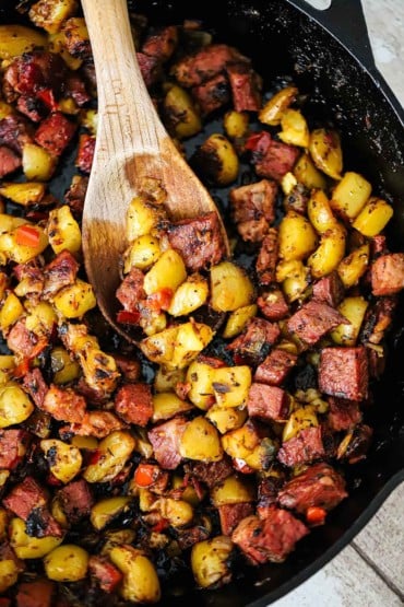 An overhead a view of a cast-iron skillet filled with corned beef hash with a large wooden spoon inserted in the middle of it all.
