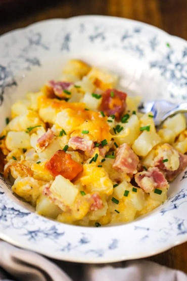 A close-up view of an antique dinner bowl filled with a serving of cheesy ham and potato casserole and topped with snipped chives.