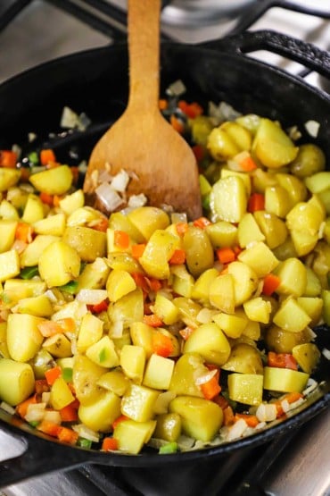 A straight-on view of a skillet filled with cubed yellow potatoes that are being cooked with chopped red bell pepper and jalapeño.