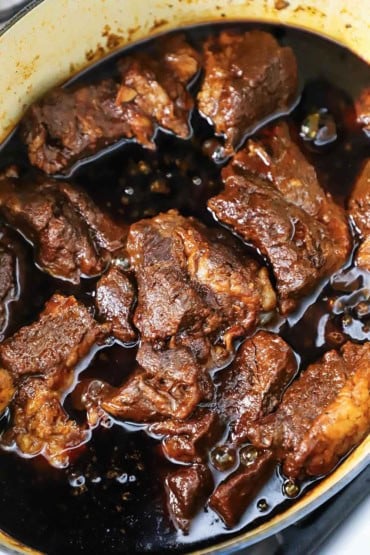An overhead view of a large oval Dutch oven filled with birria beef stew with a deep brown sauce surrounding the slow-cooked beef.