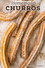 An overhead view of a homemade churros that are sitting on a platter that is filled with a sugar and cinnamon mixture.