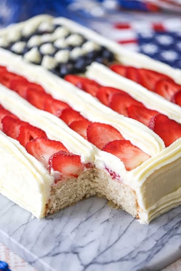 A close-up view of an American Flag Cake that has a piece cut from the corner to reveal the white cake interior.