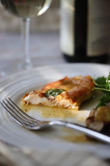 A straight-on view of a half eat chicken saltimbocca cutlet that is topped with crispy prosciutto and a fresh sage leaf.