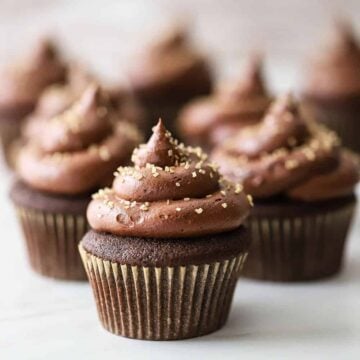 A straight-on view of chocolate cupcakes with marshmallow filling topped with gold edible glitter gems.