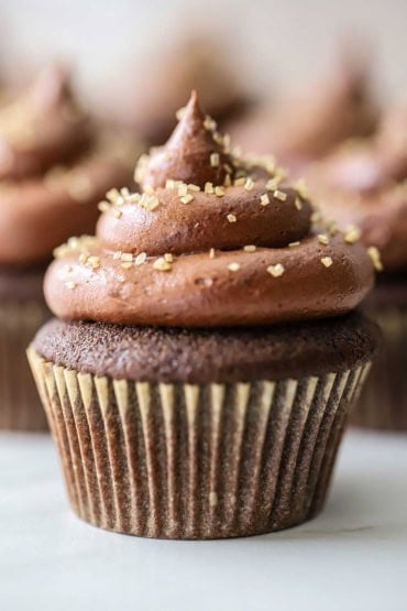 A straight-on view of chocolate cupcakes with marshmallow filling topped with gold edible glitter gems.