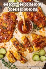 An overhead view of several pieces of hot honey chicken that are sitting the middle of a small jar filled with hot honey sauce all on crumpled brown butcher paper.