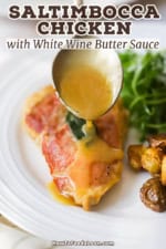 A large silver spoon being used to drizzle a white wine butter sauce over the top of a chicken saltimbocca cutlet next to roasted potatoes and an arugula salad.