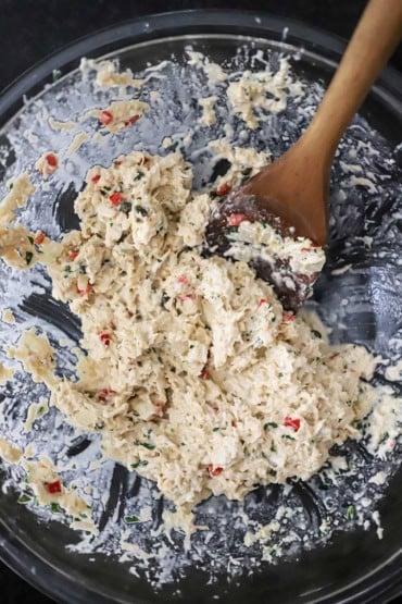 An overhead view of a crab cake mixture in a glass bowl with a wooden spatula inserted into the side of the mix.