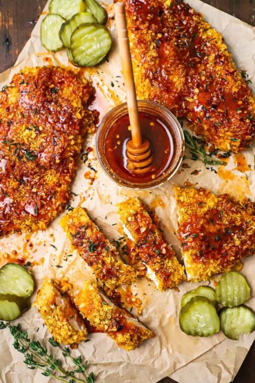 An overhead view of several pieces of hot honey chicken that are sitting the middle of a small jar filled with hot honey sauce all on crumpled brown butcher paper.