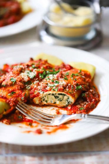 A close-up view of a half eaten spinach and cannelloni with meat sauce on the top and a fork resting on the plate.