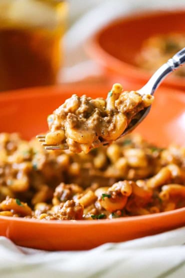 A straight-on view of a fork being raised that has a helping of homemade cheesy hamburger help on it.