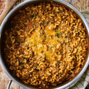 An overhead view of a large silver skillet filled with homemade cheesy hamburger helper garnished with finely chopped Italian parsley.
