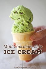 A person holding an old-fashioned ice cream cone with two large scoops of mint chocolate chip ice cream piled on top.