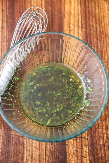 An overhead view of a medium-sized glass bowl this is filled with a homemade Italian parsley dressing.