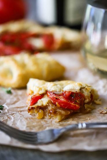 A straight-on view of a half eaten slice of a tomato galette that is layer with roasted tomatoes, gruyere cheese, and caramelized onions.